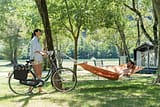 Camping La Plage Fleurie - Emplacements - Homme allongé dans un hamac et femme à vélo sur un emplacement tente en bord de rivière
