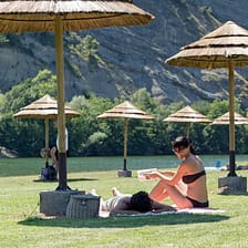Camping Plage Fleurie campsite - The beach - Young couple stretched out on the beach’s grass area, by the river