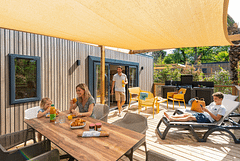 Famille profitant du soleil sur la terrasse bois d\'un mobil-home Lodge Prestige durant les vacances de printemps