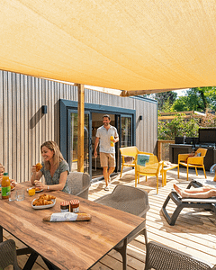 Famille profitant du soleil sur la terrasse bois d\'un mobil-home Lodge Prestige durant les vacances de printemps