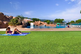 Camping Le Bois de Valmarie - Espace aquatique - Enfant allong&eacute;e sur l\'herbe au bord de la piscine