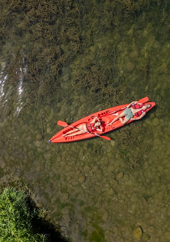 Camping Arc en Ciel - Activités - Vue zénithale d\'un couple allongé sur leur canoë rouge dans l\'Ardèche.