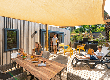 Famille profitant du soleil sur la terrasse bois d\'un mobil-home Lodge Prestige durant les vacances de printemps
