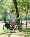 Camping La Plage Fleurie - Emplacements - Homme allongé dans un hamac et femme à vélo sur un emplacement tente en bord de rivière